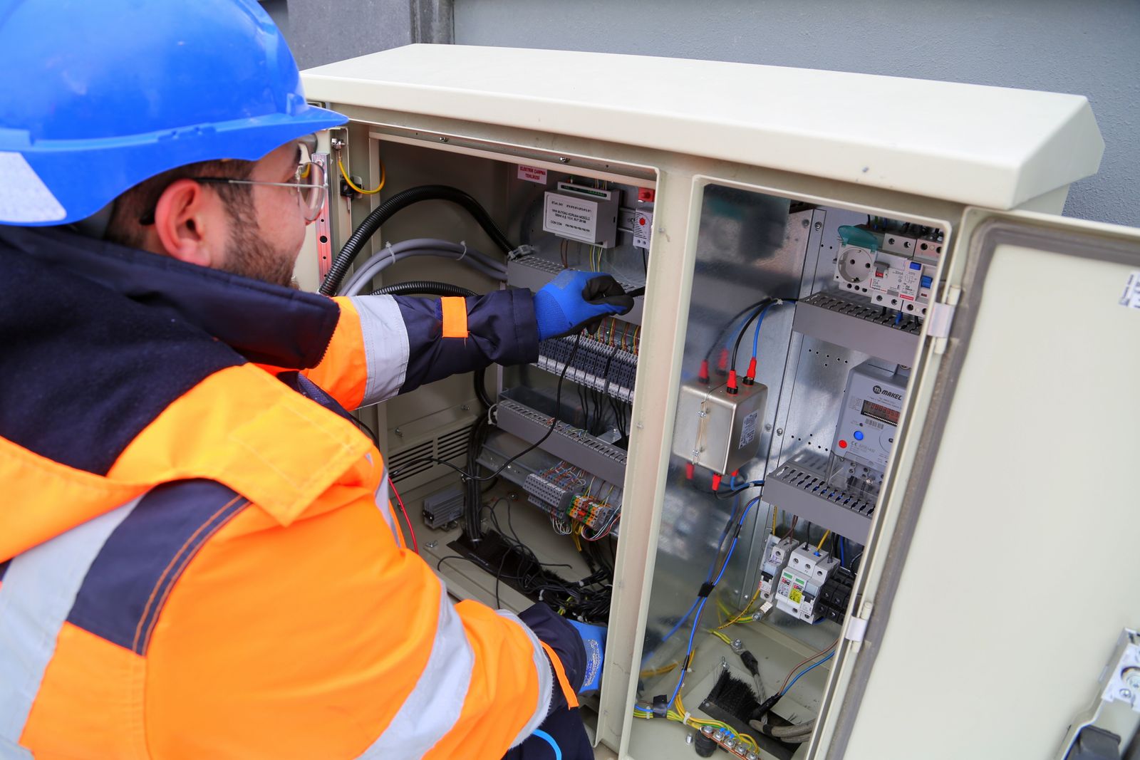 An electrician in a hard hat and high-visibility jacket working on a switchboard
